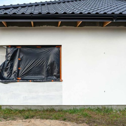 A newly applied layer of white silicone plaster on the wall of the house, the corner window is prote