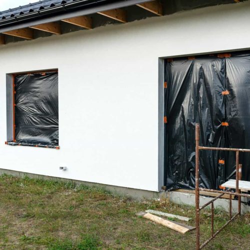 A newly applied layer of white silicone plaster on the wall of the house, visible metal scaffolding