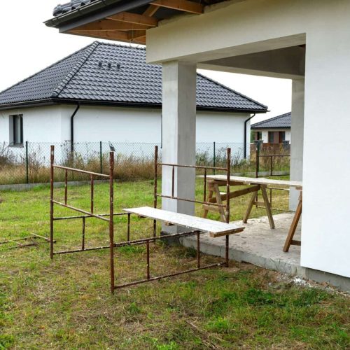 A newly applied layer of white silicone plaster on the wall of the house, visible metal scaffolding