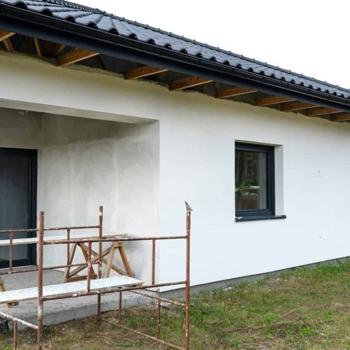 A newly applied layer of white silicone plaster on the wall of the house, visible metal scaffolding