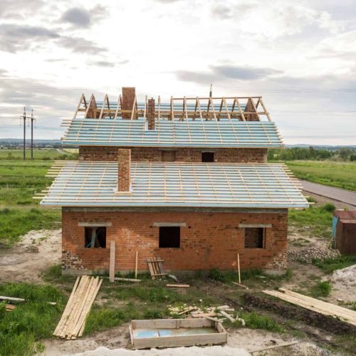 Aerial view of a brick house with wooden roof frame under construction