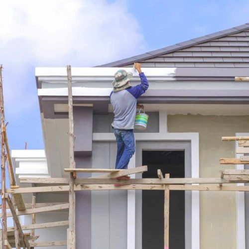 Painter on wooden scaffolding is painting roof eaves of modern house structure in construction site